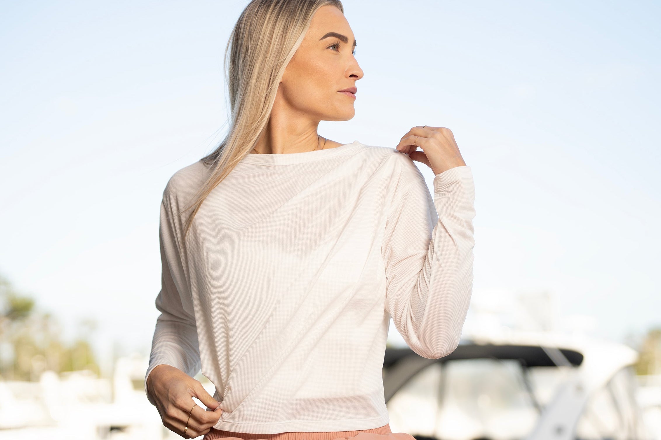 Woman in a white top and pink pants standing in front of boats at a marina.