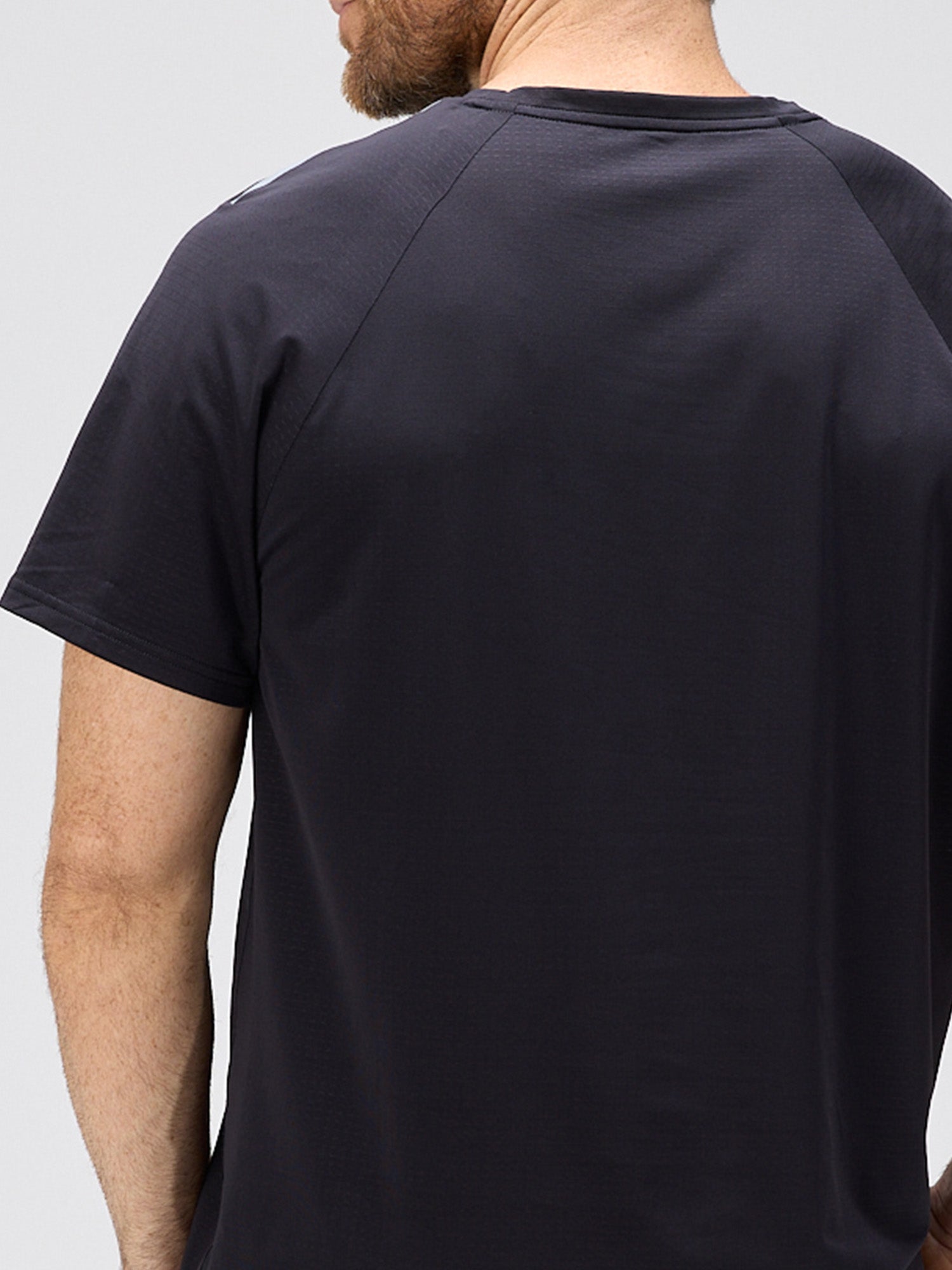 Back view of a man wearing a black lightweight tee made from moisture-wicking stretch fabric with bonded seams and horizontal ventilation perforations for padel and pickleball apparel.
