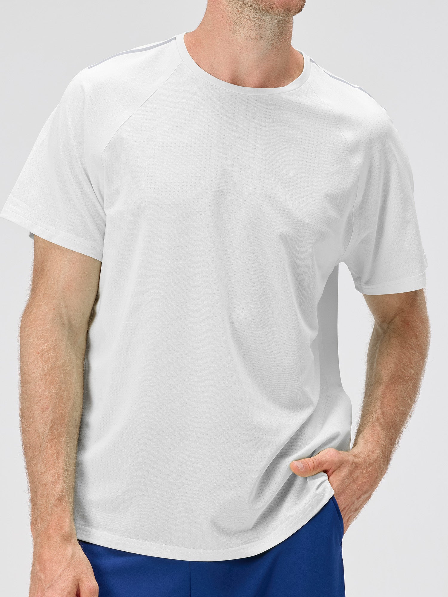 Man wearing a white lightweight moisture-wicking stretch jersey with subtle ventilation micro-perforations and bonded seams, paired with blue shorts for padel and pickleball sportswear.