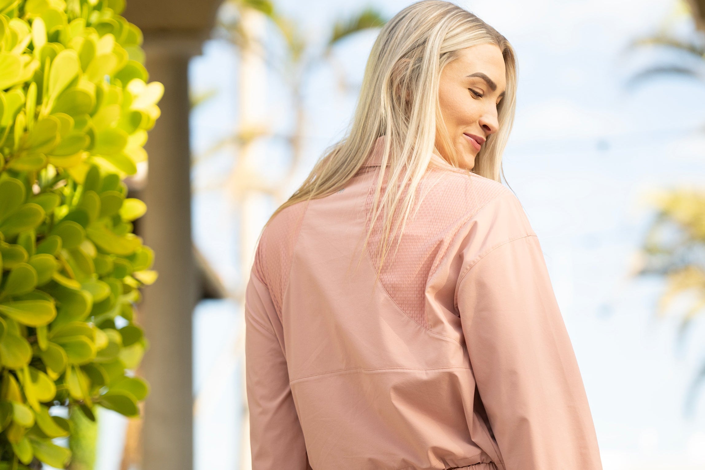 Woman in a pink outfit standing outdoors with greenery in the background