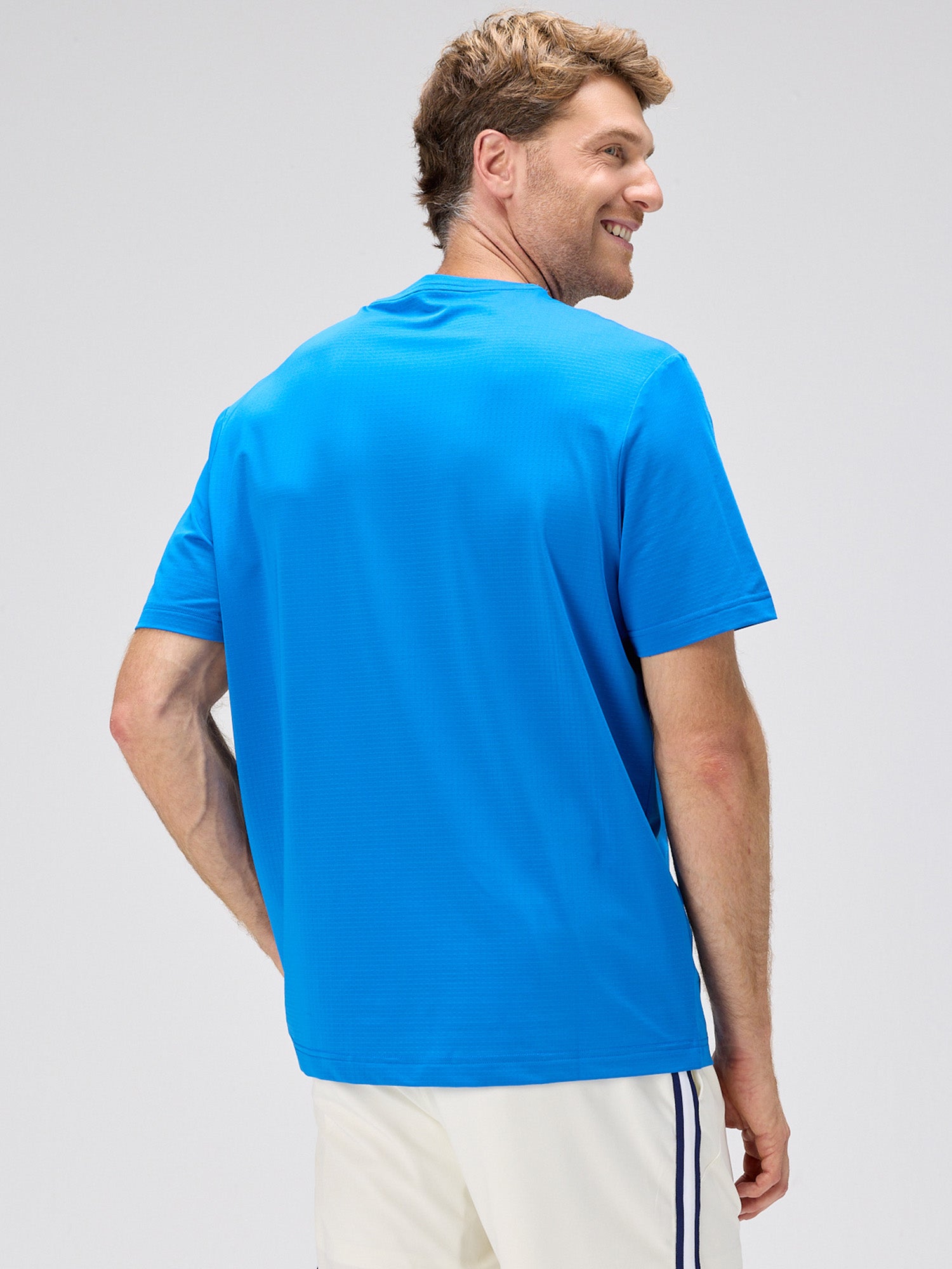 man wearing royal blue breathable athletic tee with horizontal micro perforations standing against plain background in pickleball clothing