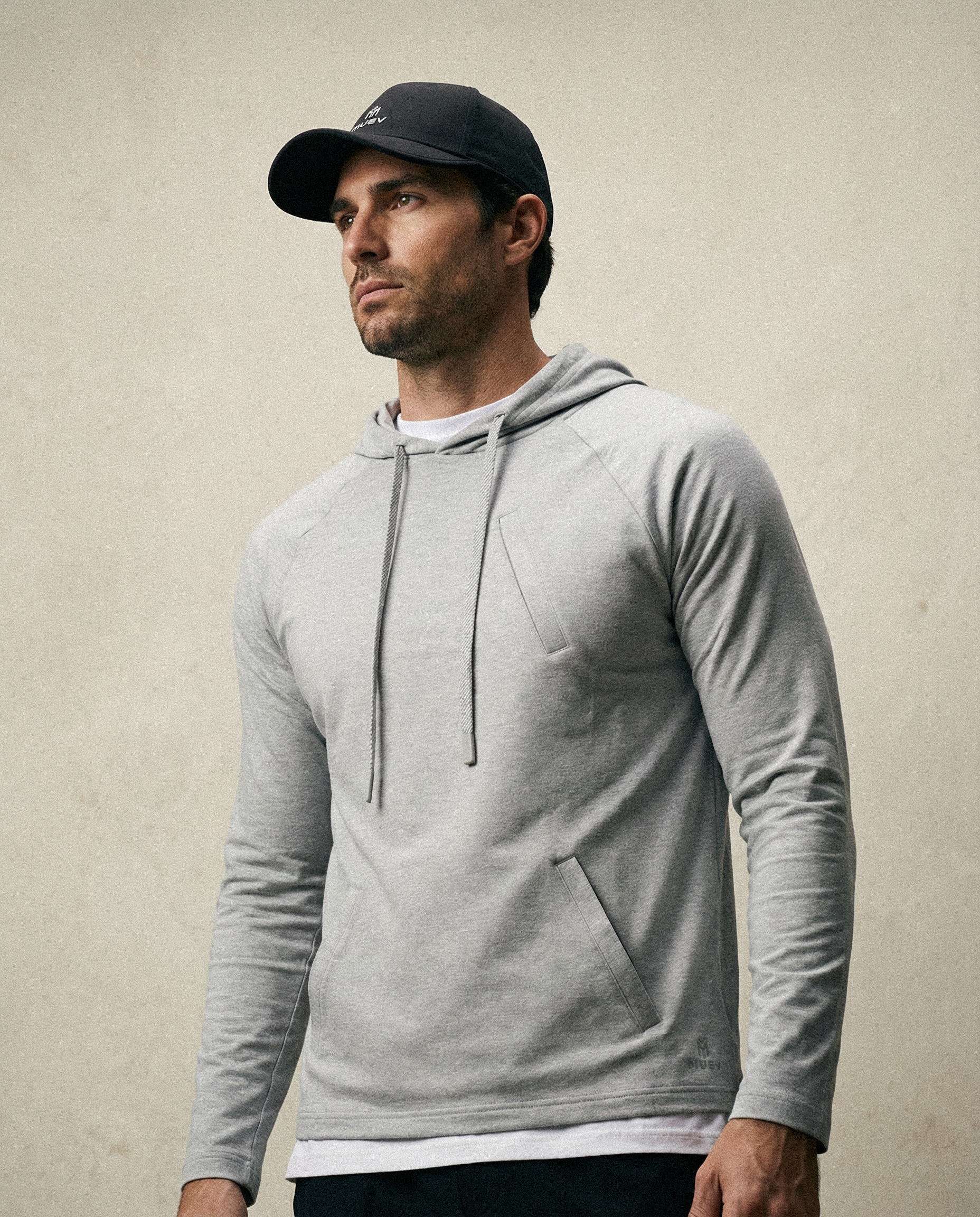 Man wearing a gray hoodie and black cap against a beige background