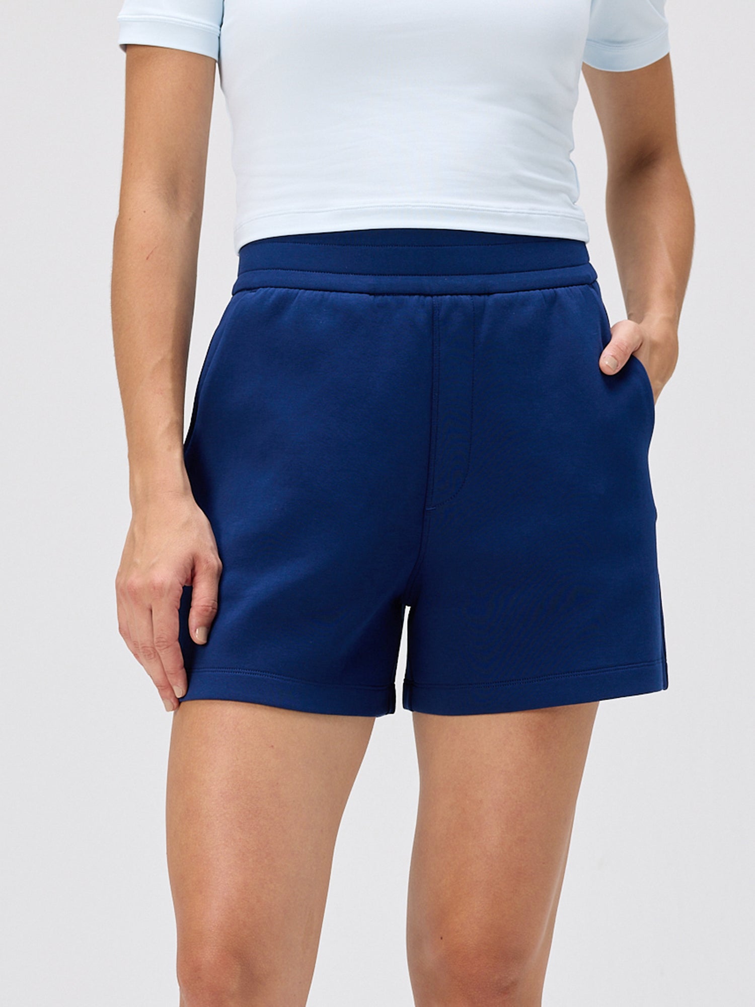 Woman wearing navy blue resort shorts with a fitted waistband and side pockets paired with a white short-sleeve top