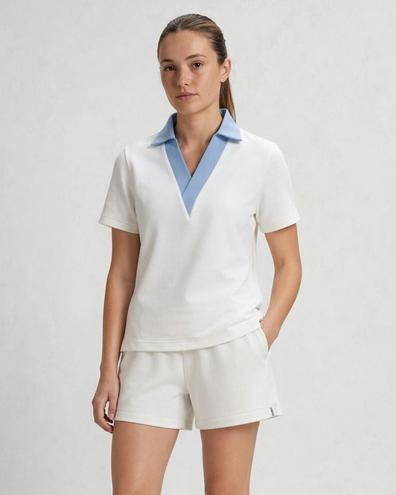 Woman wearing a white outfit with a blue collar against a plain background