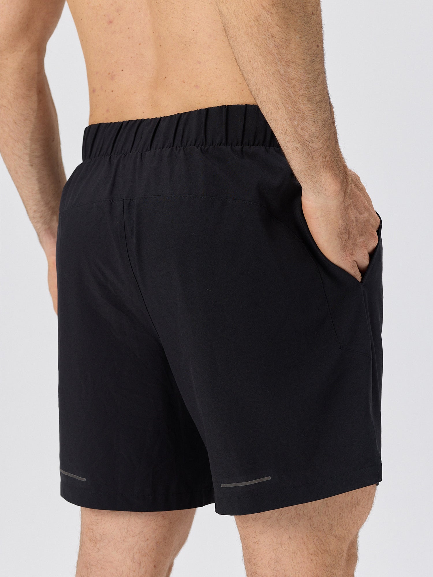 Rear view of a man wearing black lightweight athletic shorts with an elastic waistband and side pockets against a plain gray background.