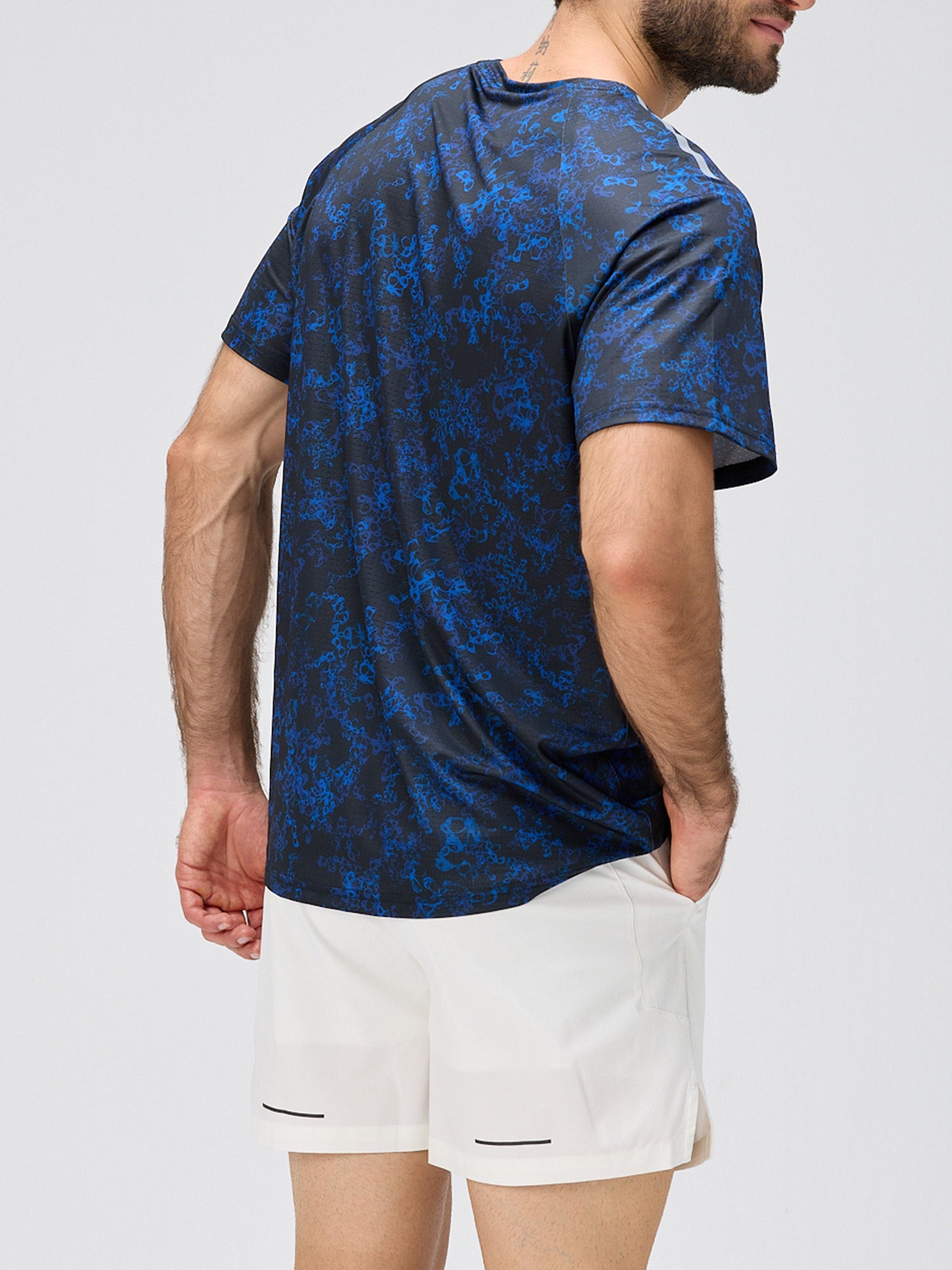 Man wearing a blue and black patterned athletic shirt paired with white shorts featuring premium stretch and a 6-inch inseam for padel and pickleball.