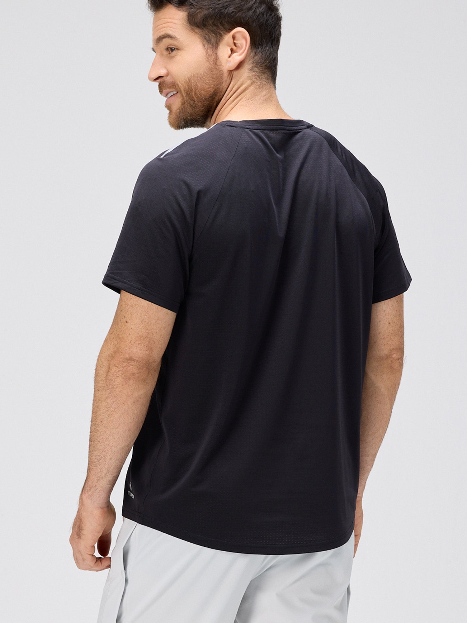 Man wearing a black lightweight performance tee with horizontal micro-perforations and moisture-wicking stretch fabric designed for padel and pickleball sportswear