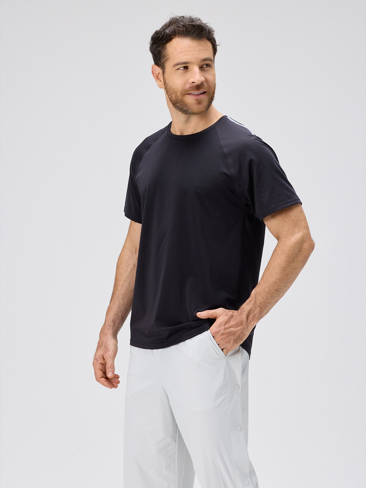 Man wearing a black lightweight performance tee made of moisture-wicking stretch jersey with horizontal micro-perforations for airflow, paired with white pants.