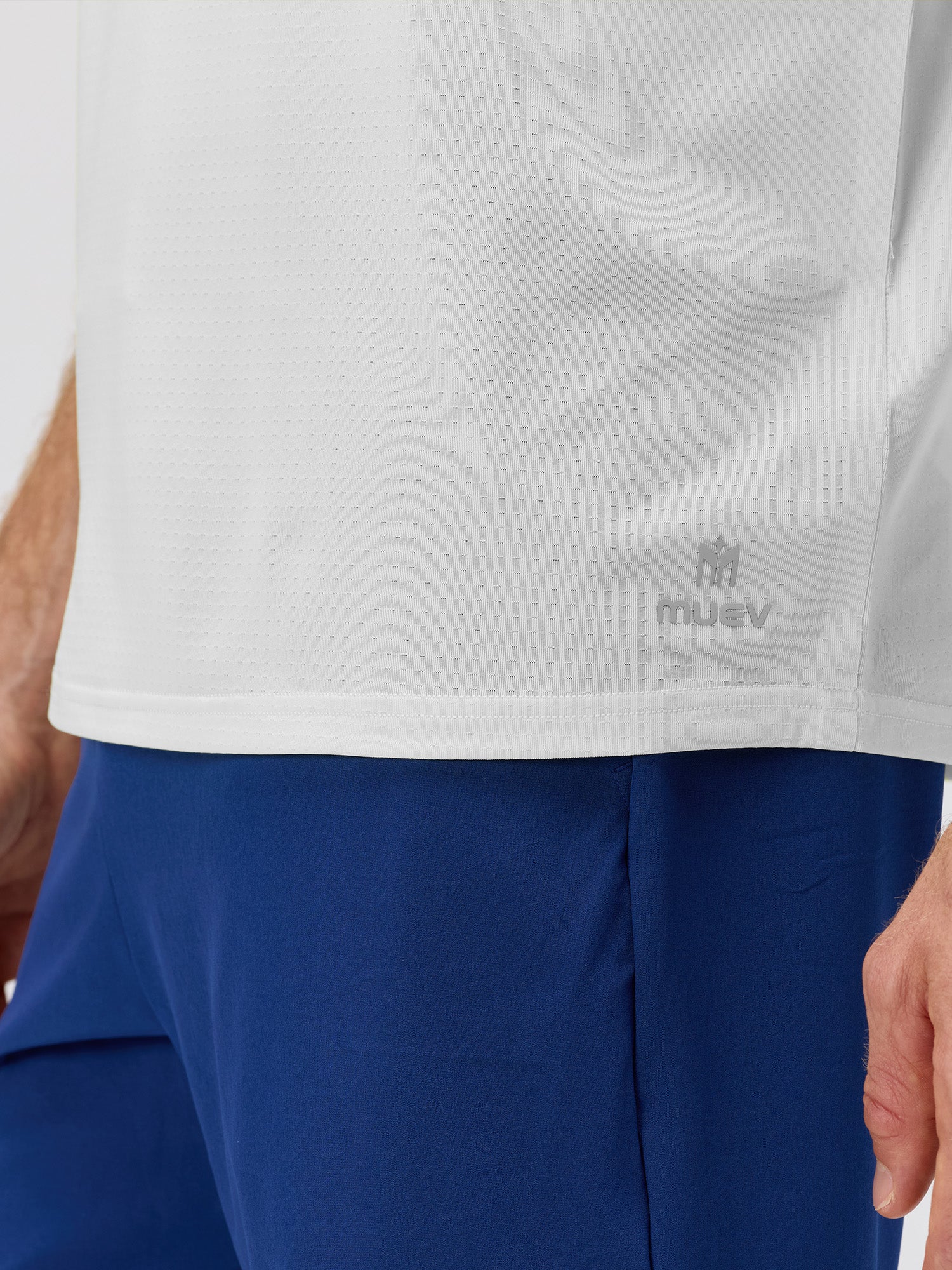 Close-up of a person wearing a white breathable athletic top with subtle perforations and a small logo above blue lightweight sports shorts.