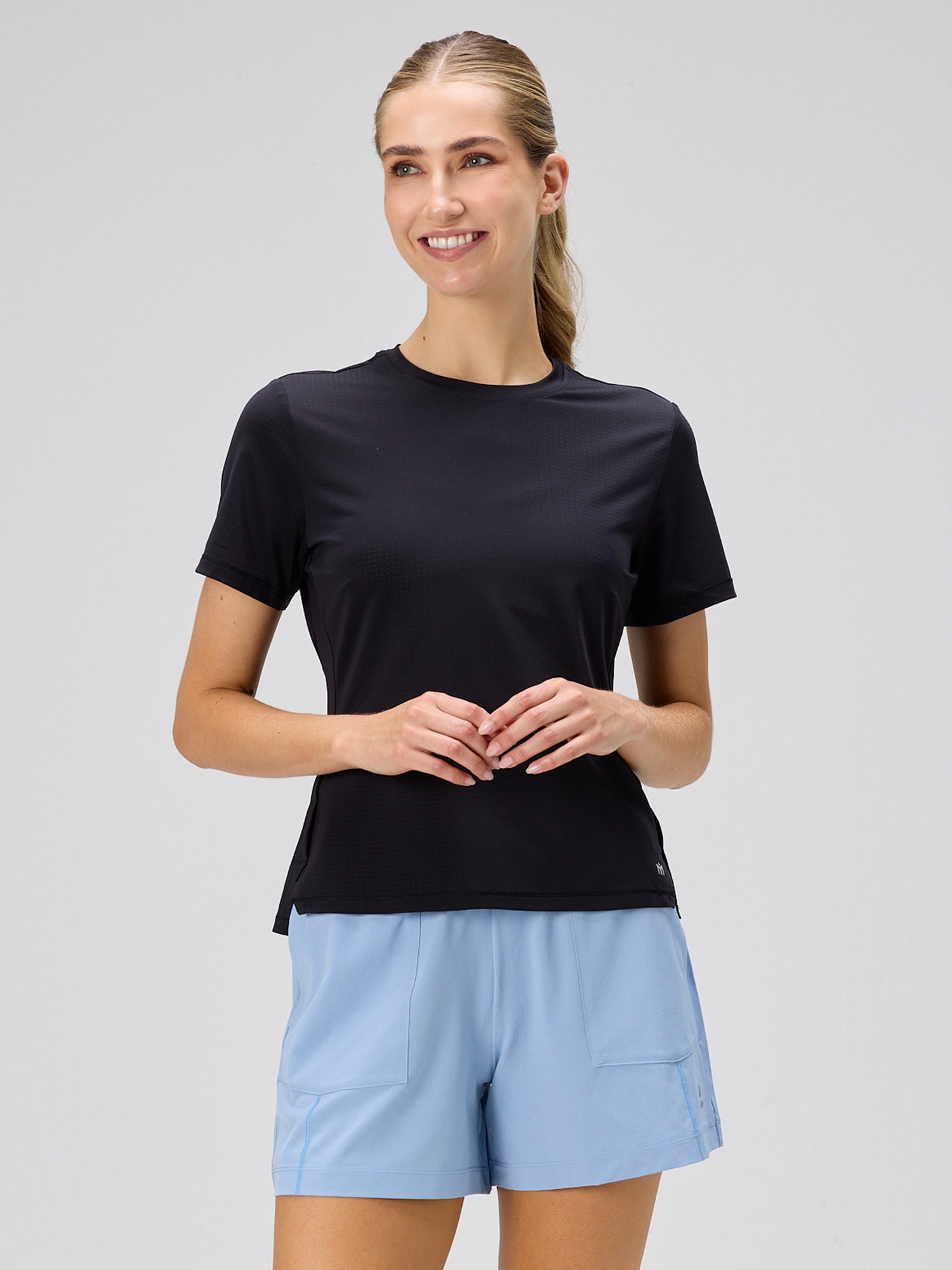 Woman wearing a black short-sleeve athletic top paired with cloud blue moisture-wicking shorts designed for padel and pickleball by MUEV