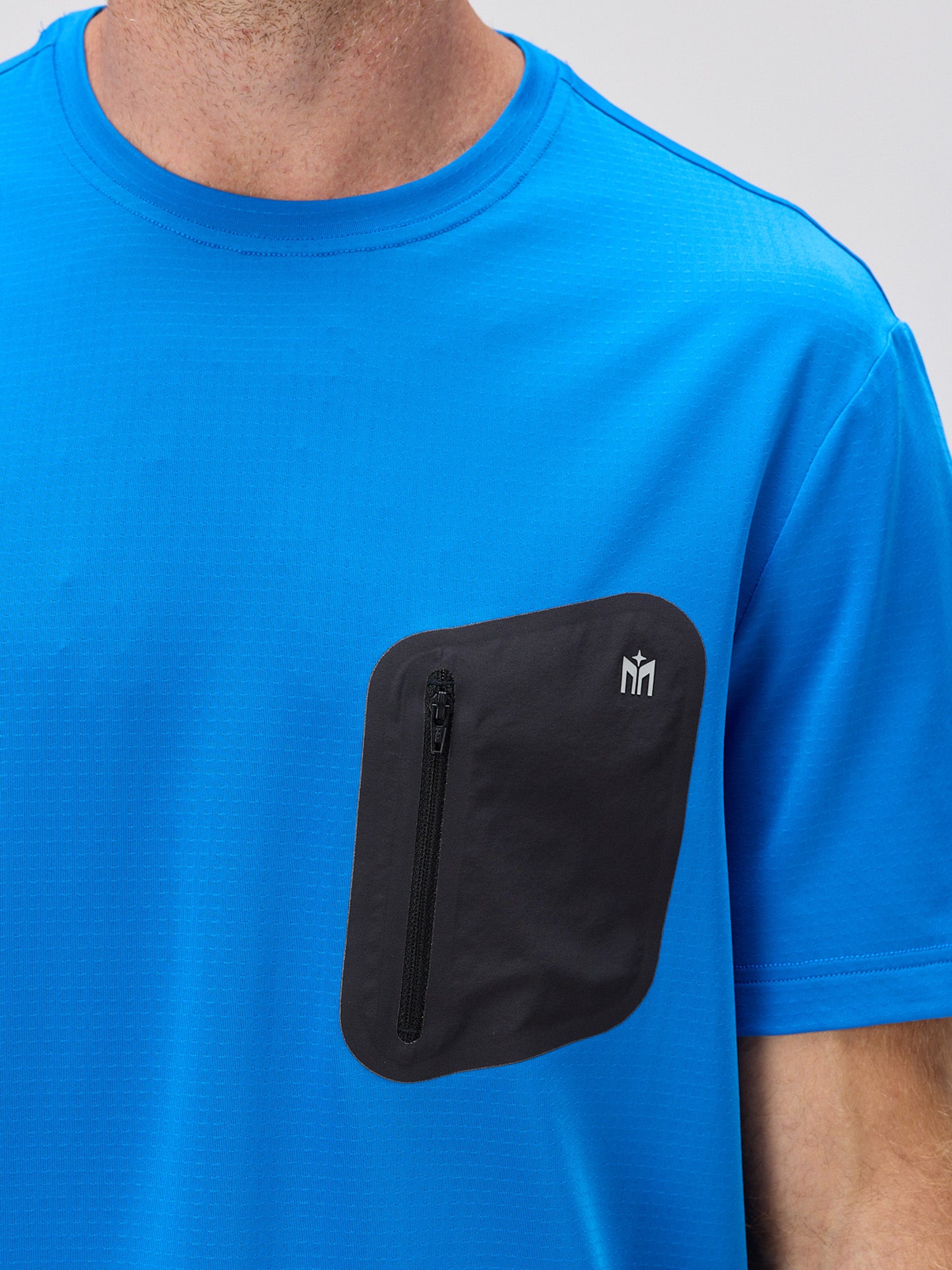 Man wearing royal blue moisture-wicking athletic shirt featuring a black zippered chest pocket with micro perforations for breathability