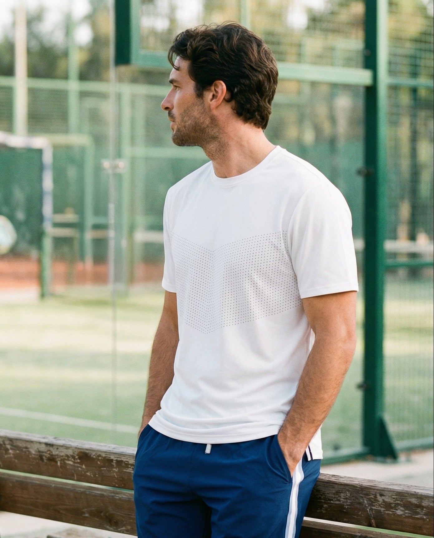Man standing on a tennis court wearing a white t-shirt and blue shorts.