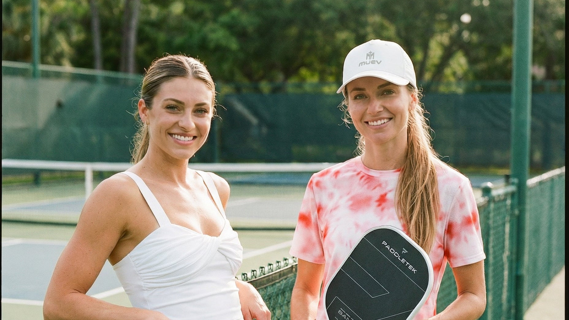 Two women on a tennis court, one holding a pickleball paddle.