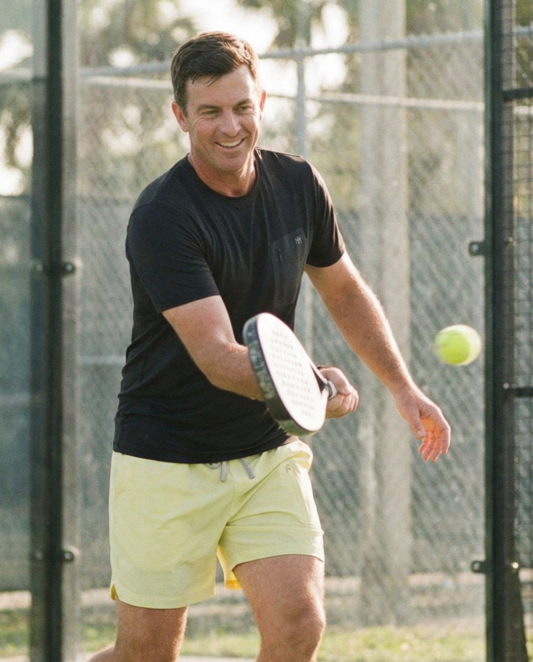 Man playing paddle tennis on an outdoor court with trees in the background