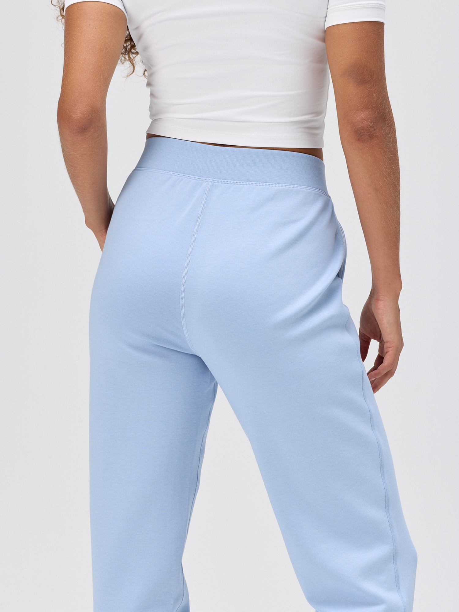woman wearing cloud blue relaxed fit pants with a wide waistband paired with a white cropped top for casual activewear