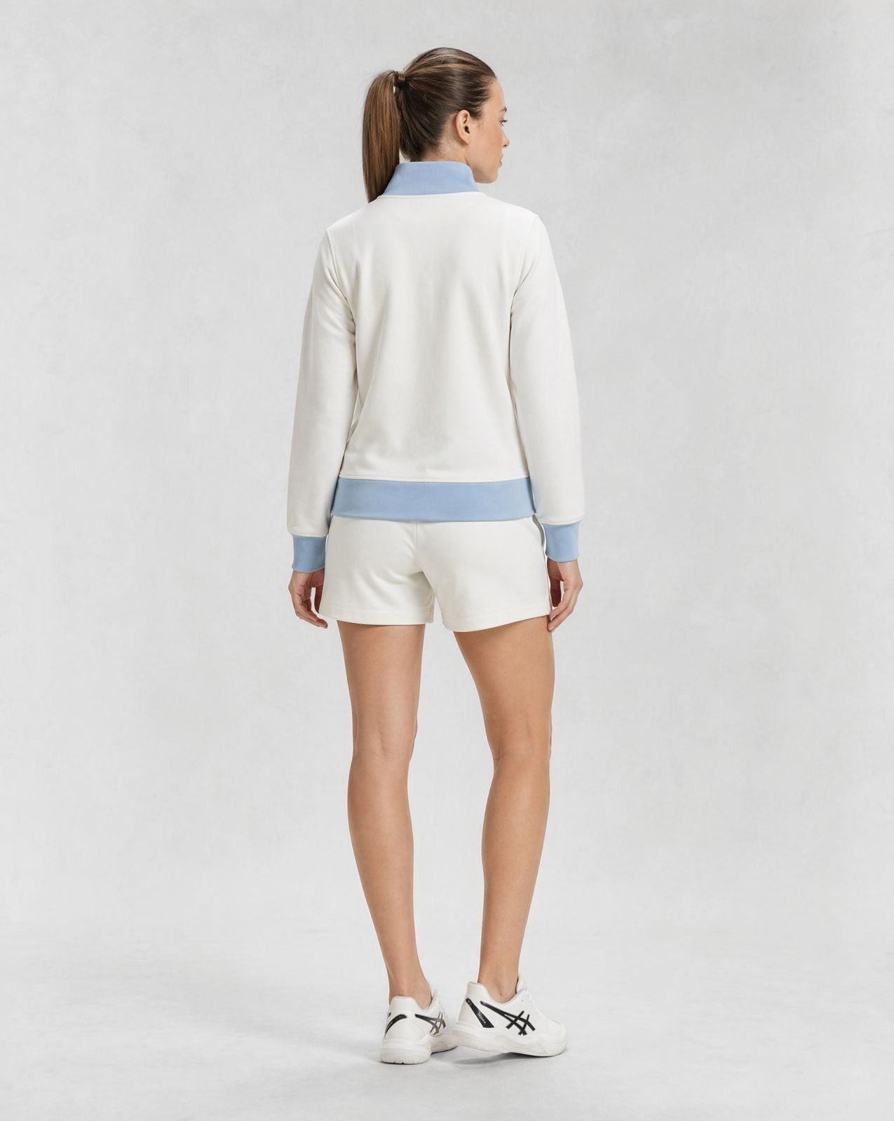 back view of white resort jacket with light blue collar and cuffs paired with matching shorts, styled for padel and pickleball clothing