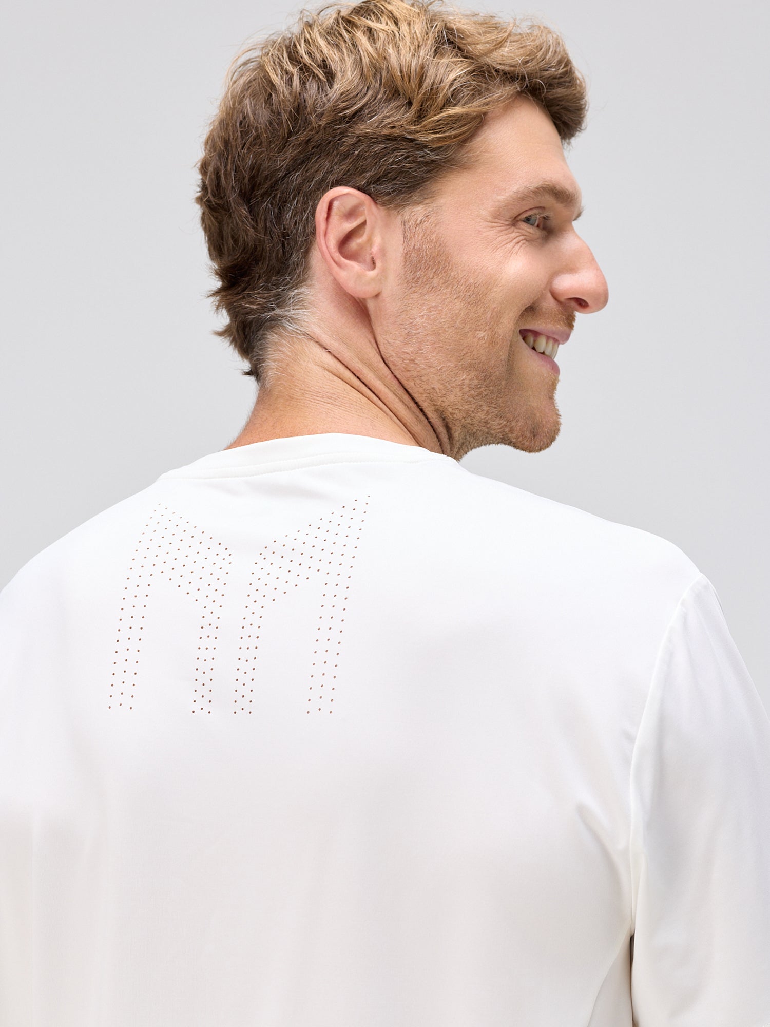 Man wearing a white lightweight shirt with perforated ventilation detail on the upper back, smiling and looking to the side.