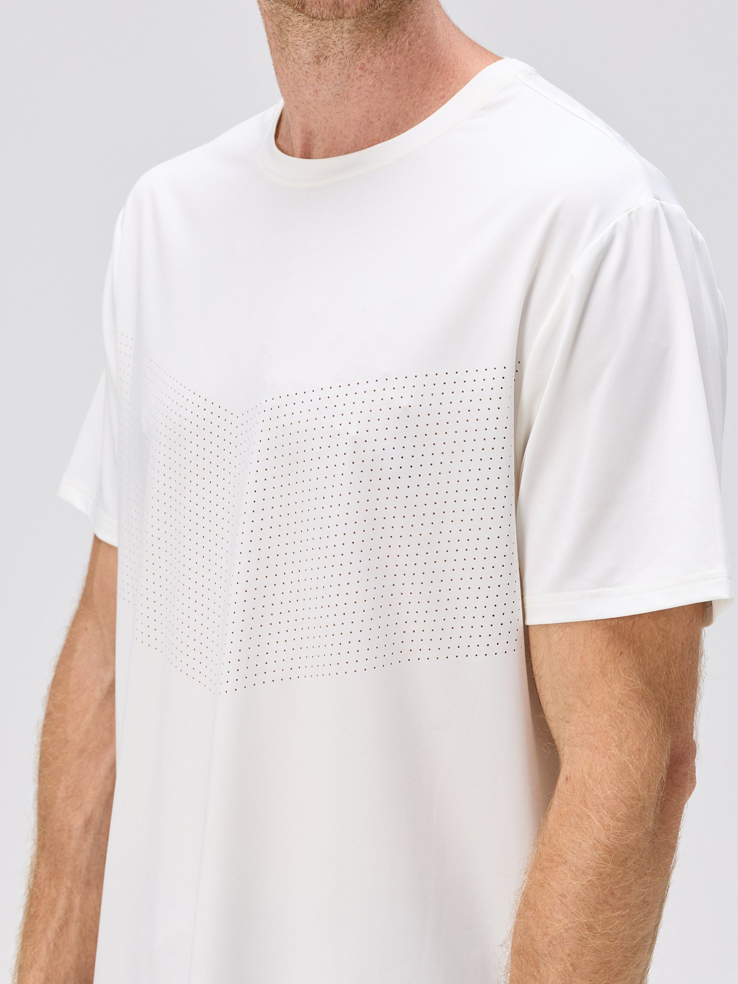 Man wearing a white short-sleeve athletic shirt with a subtle chevron pattern of small perforations across the chest for breathability.