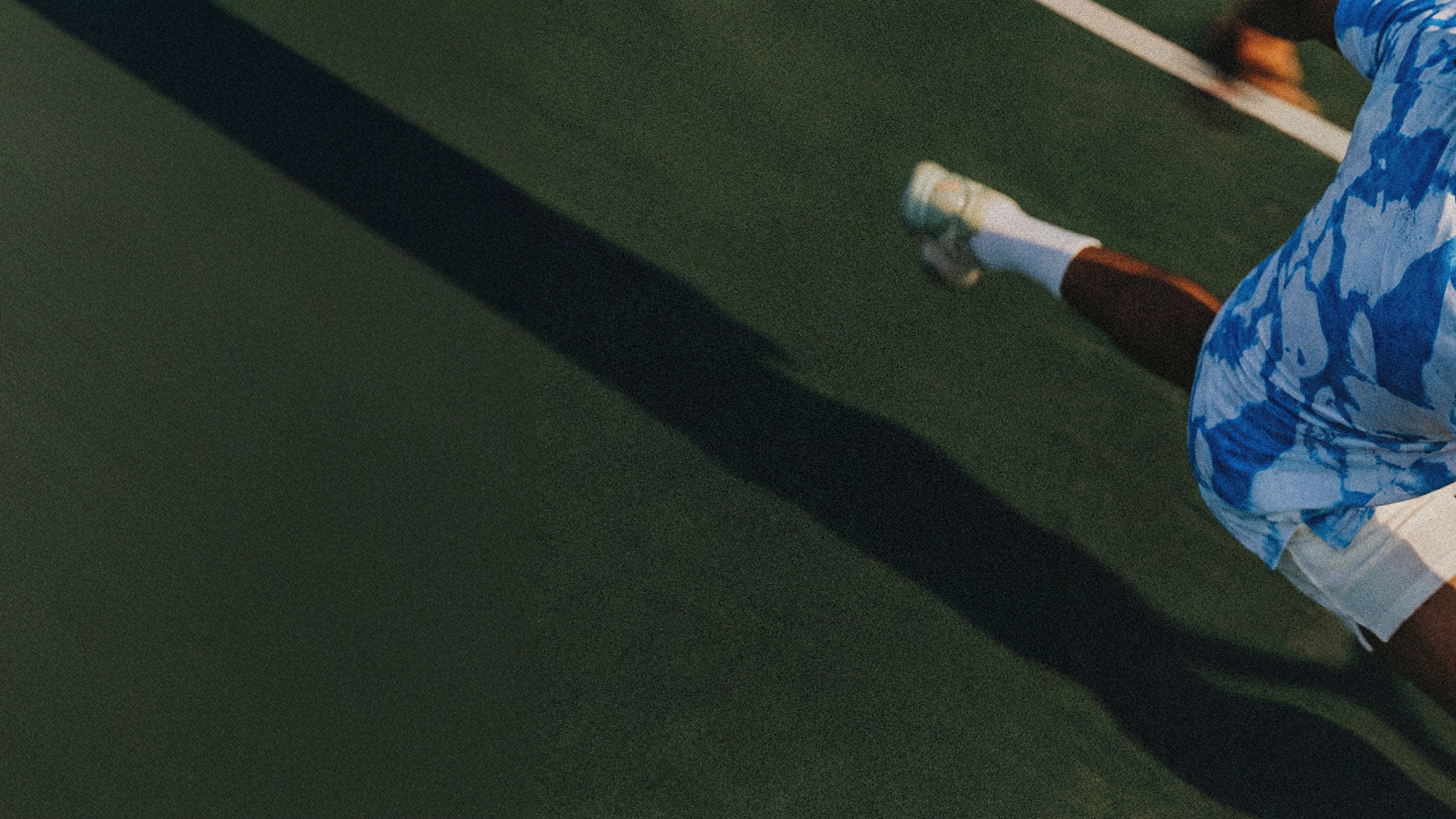 Person playing tennis on a green court with a focus on their foot and shoe.